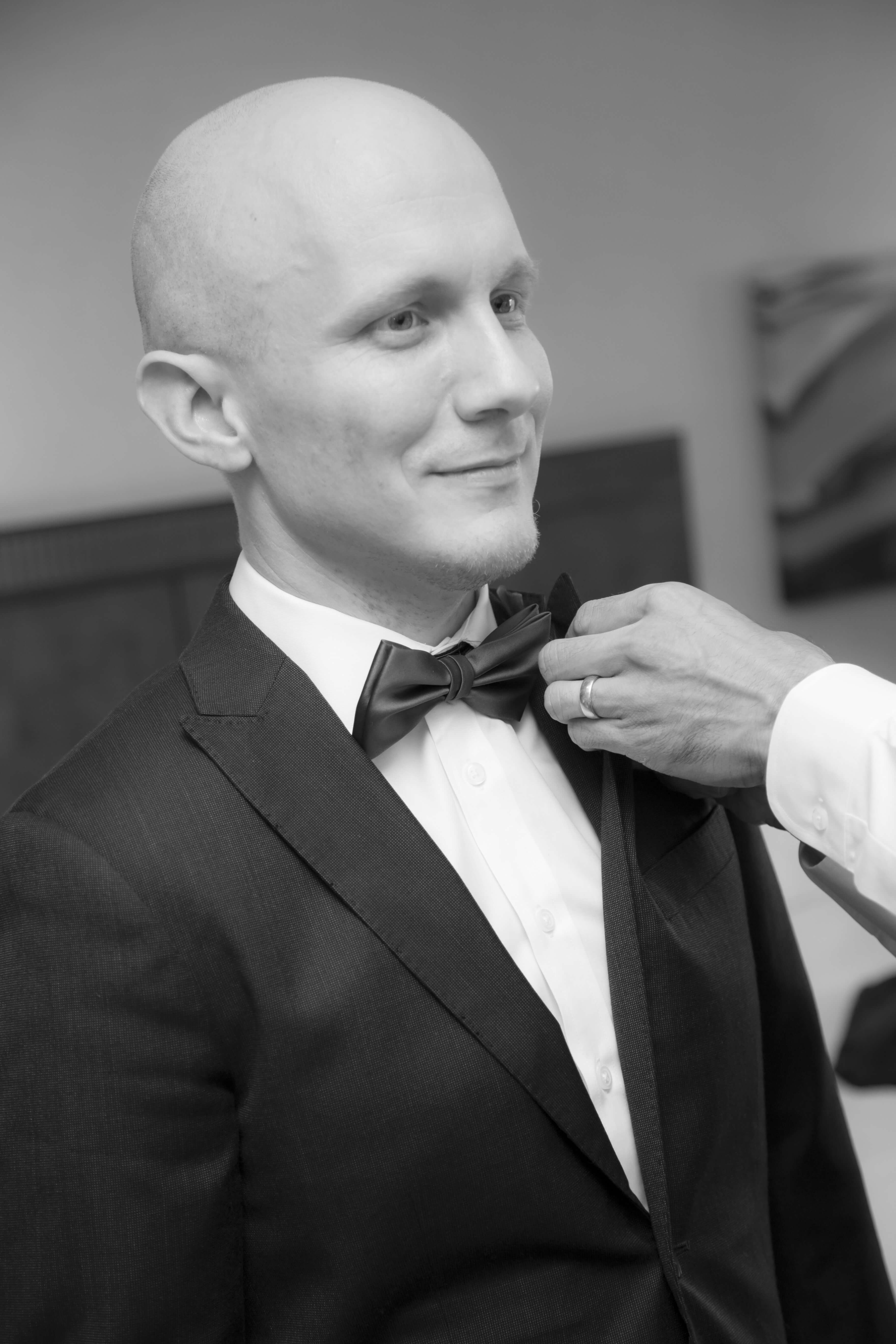 black and white photo of the groom with someone fixing his bow tie