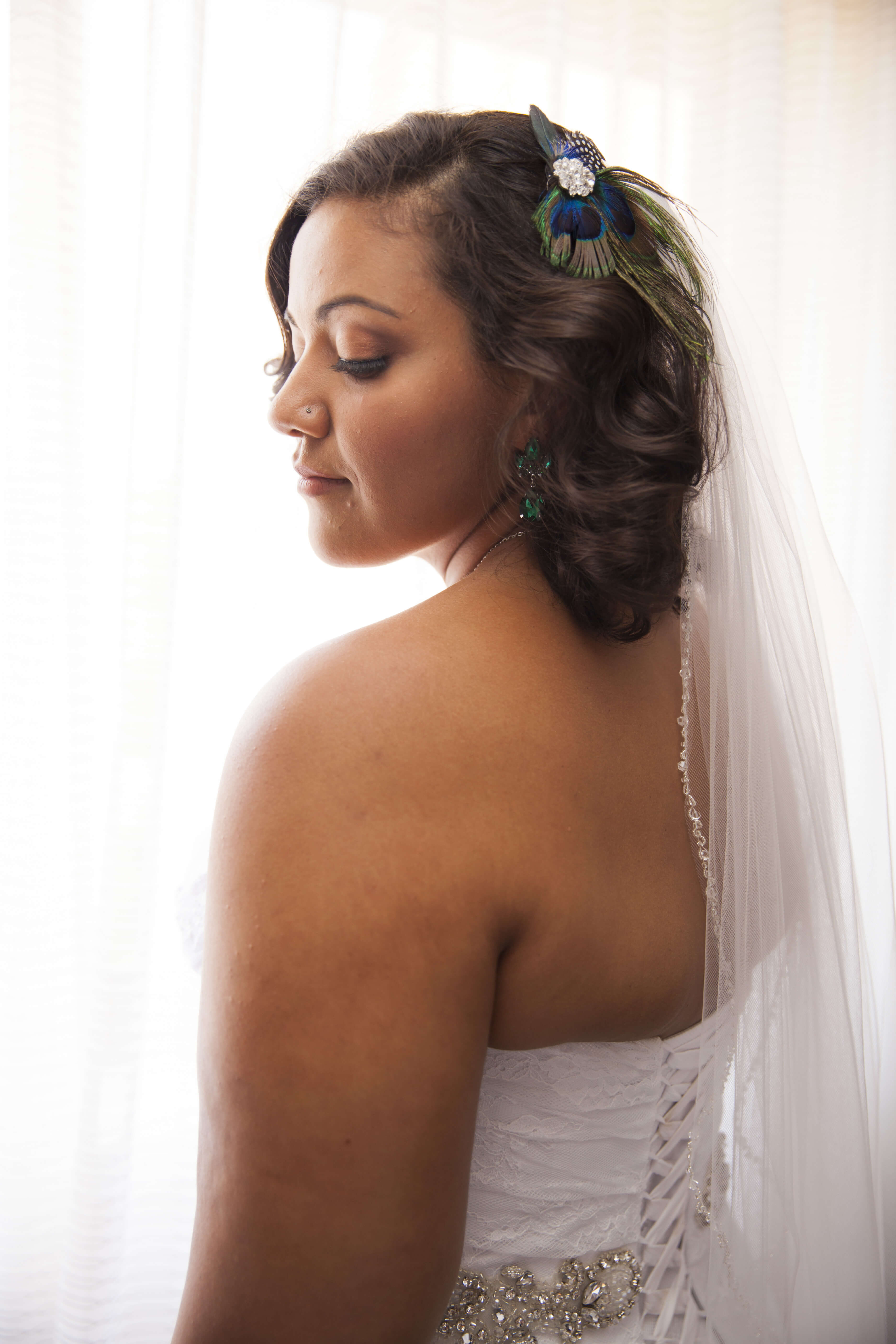 bride in a sleeveless wedding dress and a peacock feather broche on her hair 