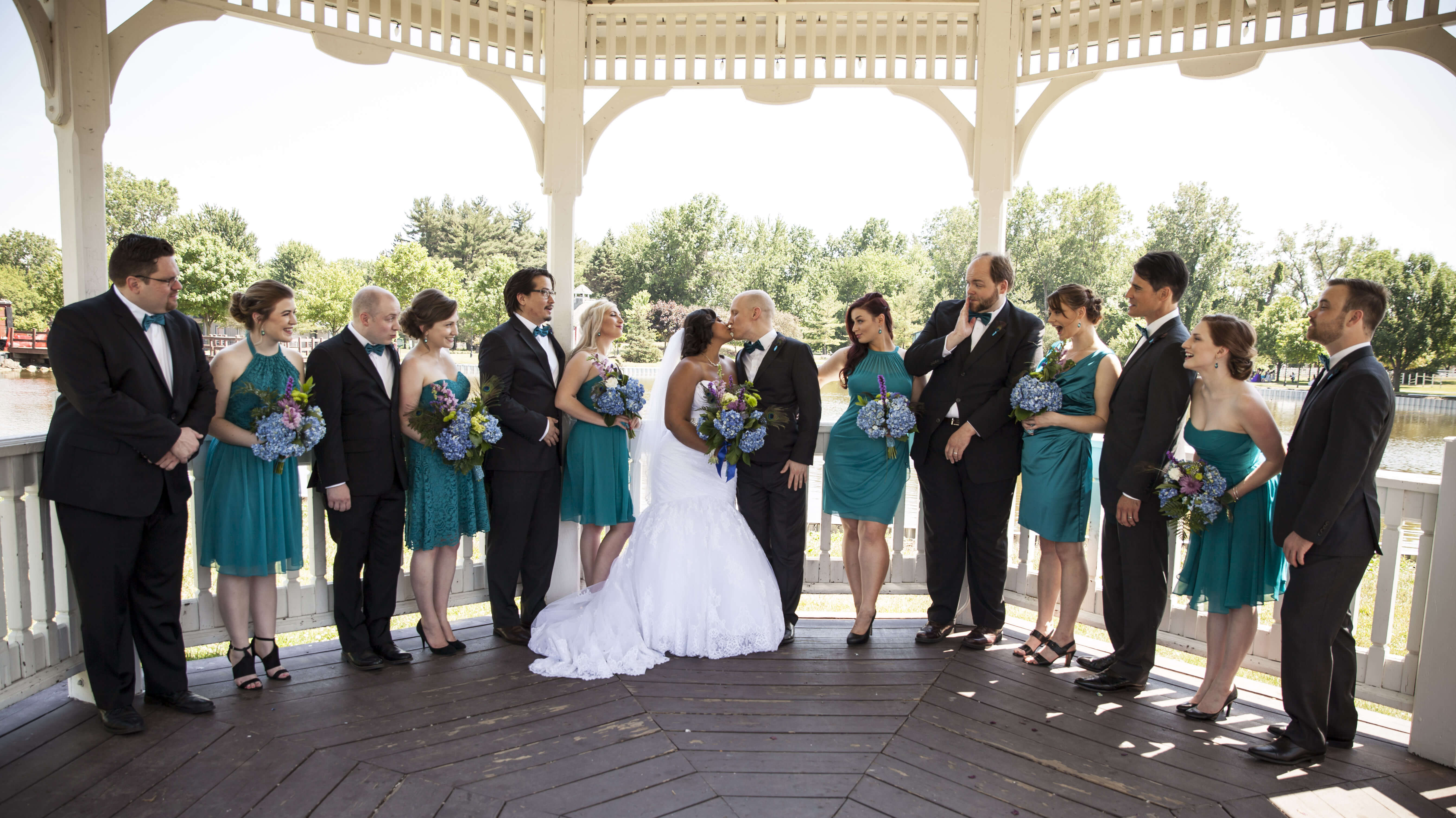 the bride and groom kissing under the gazebo with the bridal party on their sides