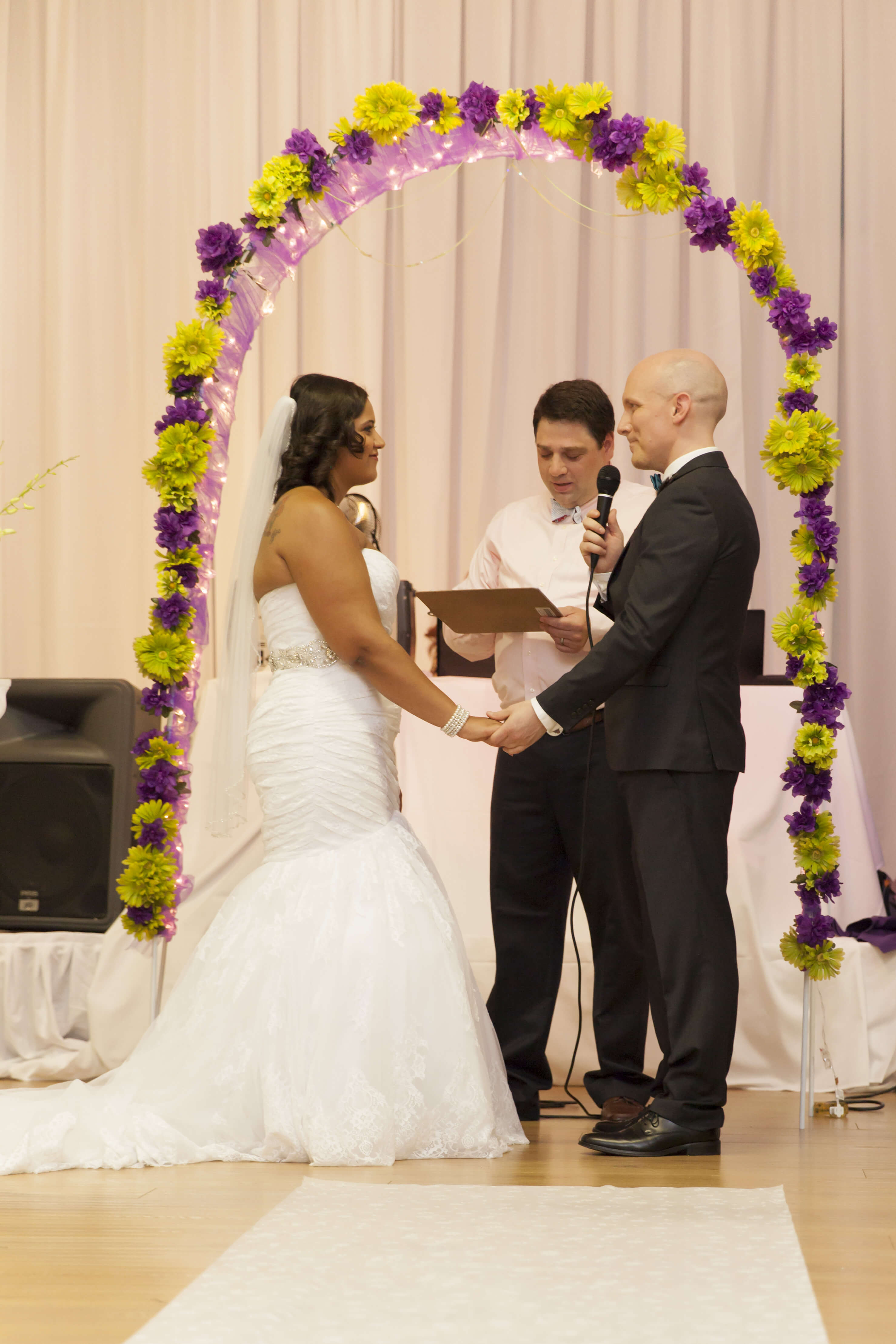 the bride and groom holding hands, facing each other at the aisle with the groom holding a microphone