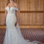Blond woman in wedding gown with dimensional lace, off-the-shoulder neckline, and bow at the back.