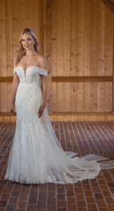 Blond woman in wedding gown with dimensional lace, off-the-shoulder neckline, and bow at the back.